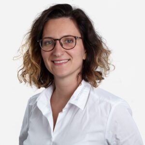 Salomea Paprotny, Sales Leader, with short curly dark hair, wearing glasses and a white shirt.